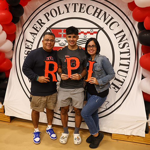 Student and parents stand in front of the RPI seal holding the letters R-P-I. 