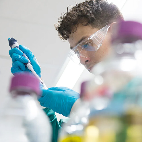 Student wearing saftey goggles and blue gloves works with a pipette